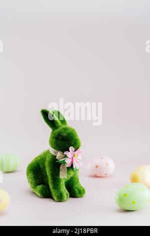 Figurina di coniglio verde e uova di pasqua colorate in diversi modelli su sfondo rosa neutro. Festive estere primavera verticale carta mockup. Selez Foto Stock