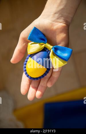 La mano della donna tiene un uovo di pollo pasquale dipinto nei colori giallo-blu della bandiera Ucraina. Vacanza al sole. Il concetto di Pasqua supporta l'Ucraina Foto Stock