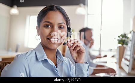 Hai chiamato il posto giusto. Ritratto di una giovane donna che utilizza una cuffia in un ufficio moderno. Foto Stock