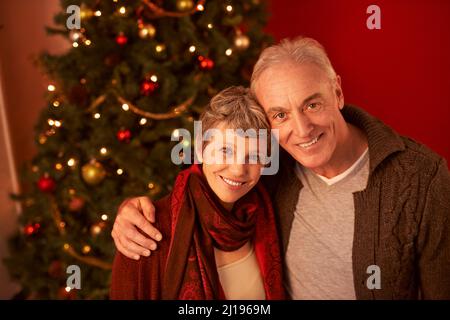 La nostra vacanza preferita. Un ritratto corto di una coppia matura felice di fronte ad un albero di Natale. Foto Stock