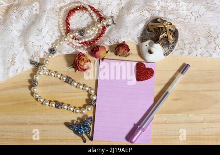 Perla Gioielleria e broccia di farfalla con pizzo e rose secche su sfondo di legno con carta bianca Foto Stock