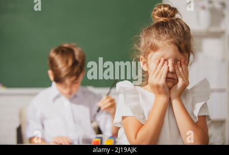 Una ragazza intelligente della scuola grida. Studentessa in uniforme coprendo il suo viso con il braccio piangendo triste di bullismo a scuola in piedi di fronte alla lavagna Foto Stock