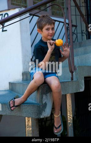 Carino ragazzo cubano mangia un papsarlo sulla scalinata di un complesso di appartamenti a l'Avana, Cuba. Foto Stock