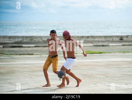 Ragazzi sYoung che giocano a calcio su una strada vicino all'oceano in Foto Stock