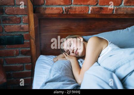Giovane donna adulta con capelli lunghi biondi che dormono sul letto in camera mansarda a casa Foto Stock
