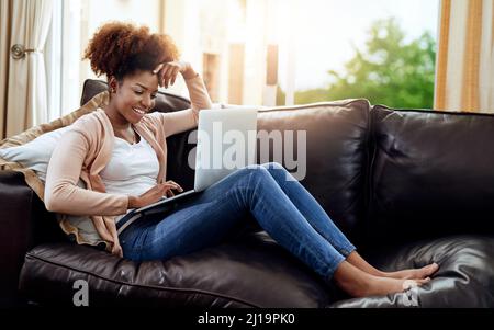 Avere una data del film solo. Scatto di una giovane donna rilassata utilizzando un computer portatile sul divano a casa. Foto Stock