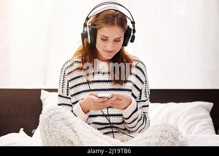 Selezionare i suoi brani preferiti. Scatto corto di una bella giovane donna che ascolta la musica a casa. Foto Stock