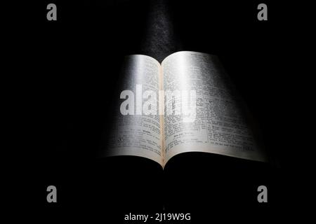 Vecchia Bibbia, libro aperto su sfondo nero, fascio di luce dall'alto Foto Stock