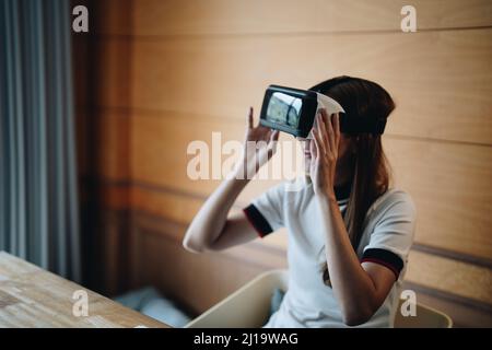 La giovane donna asiatica che indossa un visore vr è molto gioiosa e si diverta a trascorrere il tempo libero in realtà virtuale. Eccitata donna multirazziale millenaria che gioca Foto Stock