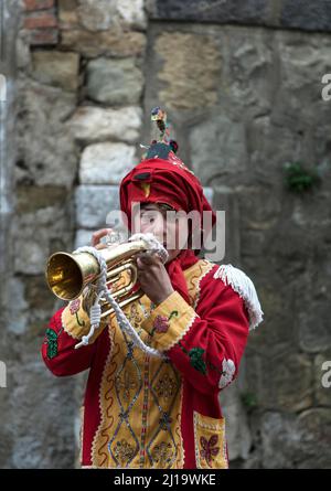 Un giovane vestito come uno dei Judei con il cappuccio rivolto verso l'alto, suonando la tromba durante il Venerdì Santo in una delle antiche strade di San Fratello, provincia di Foto Stock