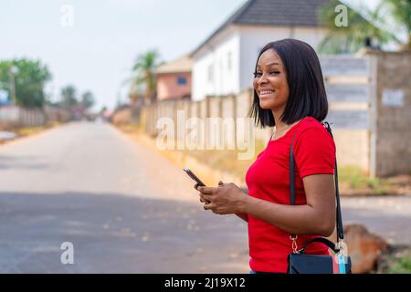 Una donna nigeriana allegra che usa il suo telefono all'aperto Foto Stock