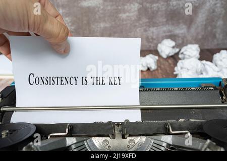 Mano tirando un pezzo di carta bianca con testo da una vecchia macchina da scrivere classica su una scrivania di legno - la coerenza è la chiave. Foto Stock