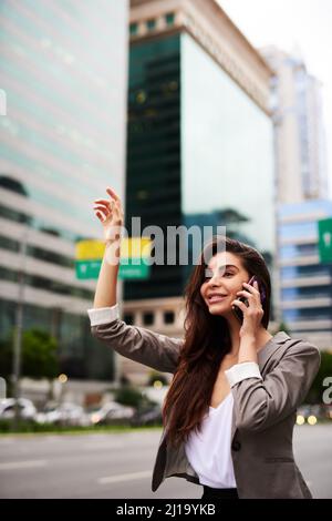 Aspetta, chiama un taxi. Scatto corto di una giovane donna d'affari attraente che si accane per un taxi mentre prende una telefonata in città durante il Foto Stock