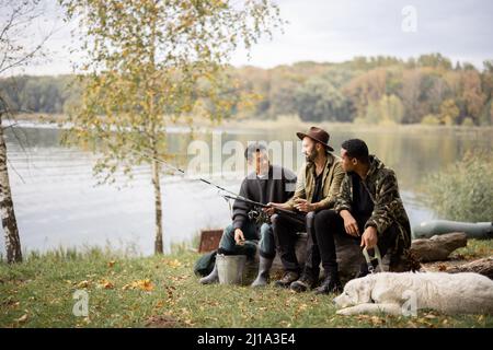 Amici maschi multirazziali che riposano e parlano in natura. Uomini dopo la pesca sul fiume o sulla costa del lago. Concetto di tempo libero e week-end nella natura. Idea di fr Foto Stock