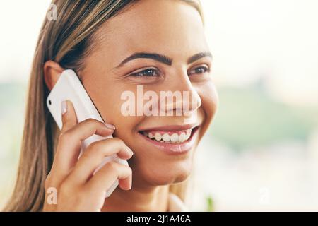Che piacevole sorpresa di parlarvi. Scatto di una giovane donna allegra che parla sul suo cellulare mentre si trova all'interno di un caffè durante il giorno. Foto Stock
