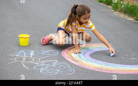 Un bambino disegna un arcobaleno sull'asfalto. Fuoco selettivo. Capretto. Foto Stock