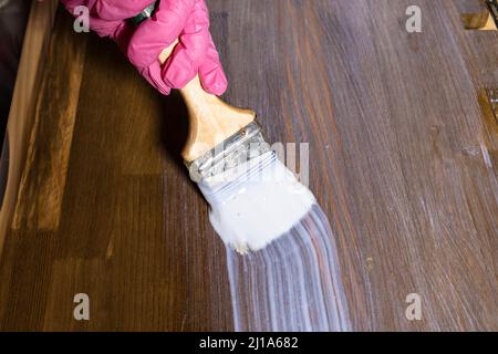 la mano gloved vernicie un asse di legno macchiato nel paese Foto Stock