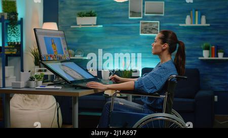 Donna con disabilità che modifica le immagini sul touch screen e utilizzando un tablet grafico con stilo. Fotografa non valido che ritoccano le foto sull'app del computer mentre si è seduti in sedia a rotelle. Foto Stock