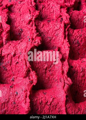 Gelato al ribes nero congelato - dettaglio telaio completo del sorbetto. Primo piano di una superficie rossa di gelato riempito con pezzi di frutta mista. Foto Stock