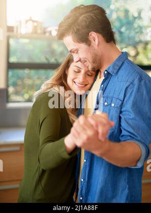 L'amore mette il cuore in una casa. Shot di una giovane coppia affettuosa ballando mano in mano insieme nella loro cucina. Foto Stock