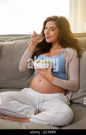 Sano per me, sano per il bambino. Shot di una donna incinta che mangia un'insalata sana a casa. Foto Stock