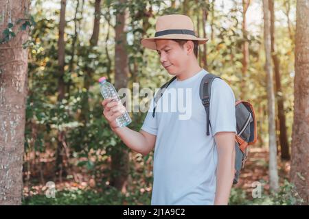 Un turista maschio che trasporta una borsa, una bottiglia d'acqua e una macchina fotografica cammina attraverso la foresta. Foto Stock