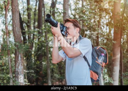 Un turista maschio che trasporta una borsa, una bottiglia d'acqua e una macchina fotografica cammina attraverso la foresta. Foto Stock