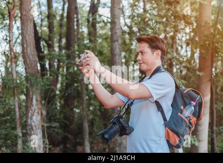 Un turista maschio che trasporta una borsa, una bottiglia d'acqua e una macchina fotografica cammina attraverso la foresta. Foto Stock