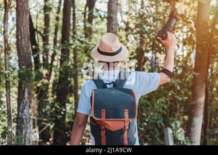 Un turista maschio che trasporta una borsa, una bottiglia d'acqua e una macchina fotografica cammina attraverso la foresta. Foto Stock