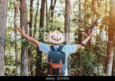 Un turista maschio che trasporta una borsa, una bottiglia d'acqua e una macchina fotografica cammina attraverso la foresta. Foto Stock