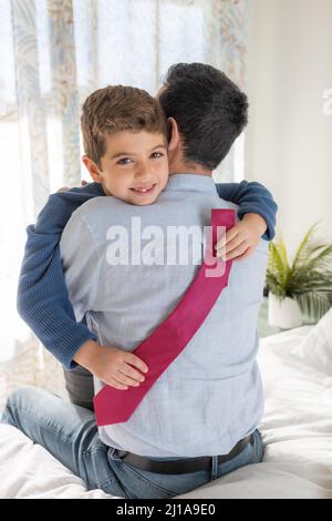 Figlio che abbracciava il padre con una cravatta sulle mani Foto Stock