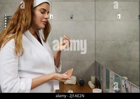 Bella donna giovane incinta che prende le pillole con la bellezza e gli integratori di salute, avendo alimentazione di dieta, in piedi nel bagno di casa Foto Stock