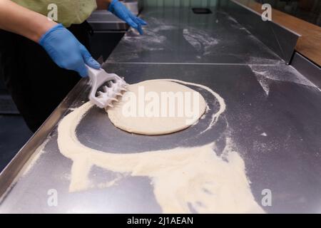 Il cuoco lavora la pasta per pizza con uno speciale rullo con punte per rendere la pasta soffice e croccante. Foto Stock