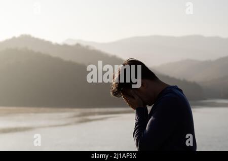 L'uomo depresso miserabile asiatico si distingue da solo con la montagna e il lago sfondo. Depressione e concetto di salute mentale. Foto Stock