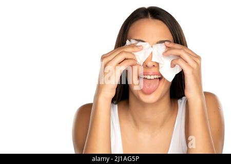 giovane donna divertente pulisce il suo viso con salviette bagnate su sfondo bianco Foto Stock