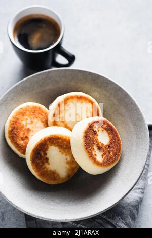 Frittelle di formaggio in ciotola artigianale in ceramica servita con una tazza di caffè espresso, vista dal primo piano. Cibo per la colazione Foto Stock