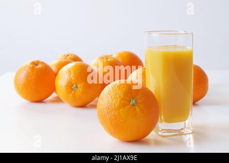 Un bicchiere di succo d'arancia appena spremuto e un gran numero di arance giacciono sul tavolo in modo che ogni mattina sia decorata con un colore arancione luminoso, Foto Stock