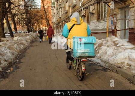 Mosca, Russia - 25 febbraio 2022: Corriere di Yandex lavka su ciclomotore artigianale consegna generi alimentari e giri sul marciapiede in inverno Foto Stock