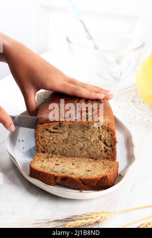 Donna che taglia pane di Banana appena sfornato su tavola bianca di legno Foto Stock