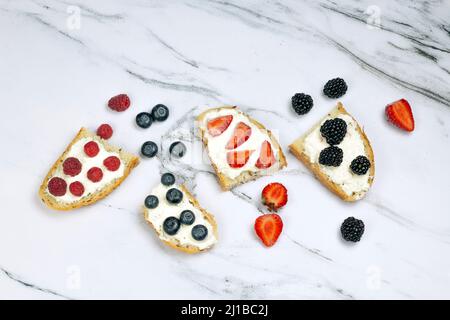 Pane tostato gustoso con formaggio cremoso, fragola, lampone, mora e mirtillo su sfondo di marmo bianco. Mattina, concetto di colazione, vista dall'alto, Foto Stock