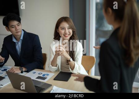 I progettisti di workgroup aziendali diversi collaborano con una donna leader asiatica per discutere i dati statistici dei report finanziari cartacei, prevedendo di lavorare su comune Foto Stock