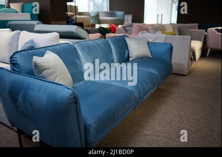 Elegante e minimalista divano in velluto blu con cuscini grigio chiaro, in vendita nello showroom del negozio di mobili. Mostra di arredi morbidi Foto Stock