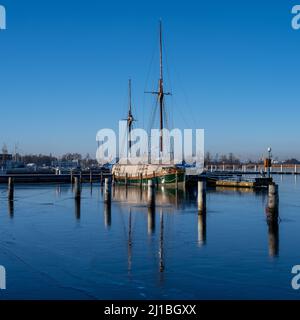 Una barca a vela in un porticciolo chiusa per l'inverno. Acqua blu e cielo blu chiaro Foto Stock