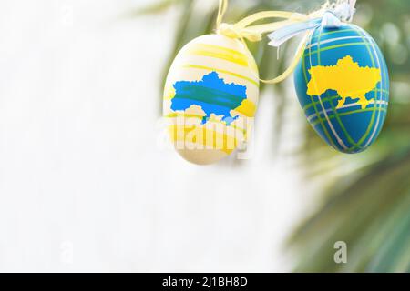 Uova di Pasqua giallo e blu con una mappa disegnata di Ucraina appesa su un ramoscello nell'aria fresca. Buone vacanze. Foto Stock