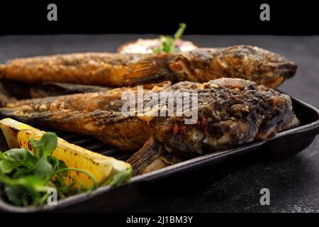 Pesce fritto Gby del Mar Nero, con limone ed erbe, su sfondo scuro Foto Stock