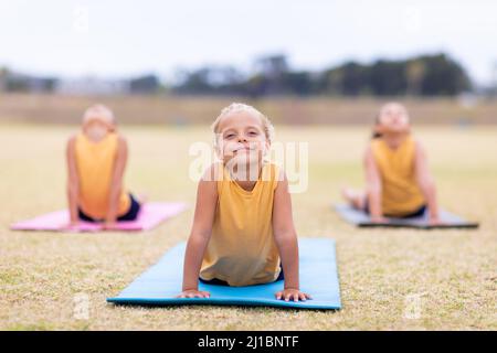 Le studentesse multirazziali elementari che fanno il cane rivolto verso l'alto pongono l'esercizio sul tappeto yoga Foto Stock