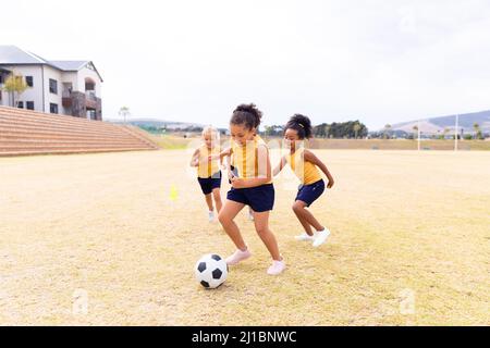 Scuole elementari multirazziali in uniforme sportiva giocando a calcio a scuola contro il cielo Foto Stock