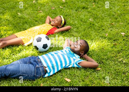 Sorridente ragazzo e ragazza afroamericana sdraiato con le mani dietro la testa da pallone di calcio nel cortile Foto Stock