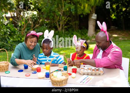 Ragazza e ragazzo afroamericano con nonni che indossano orecchie conigliere e dipingono uova il giorno di pasqua Foto Stock