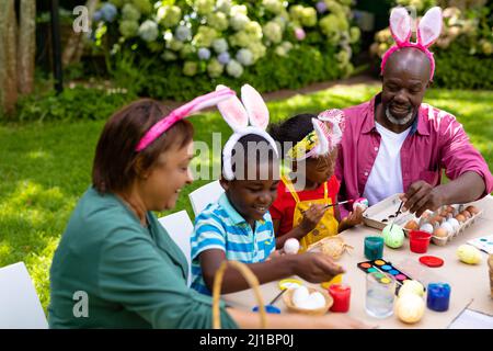 Felice afroamericano fratelli e nonni in coniglietto orecchie dipingere uova il giorno di pasqua Foto Stock